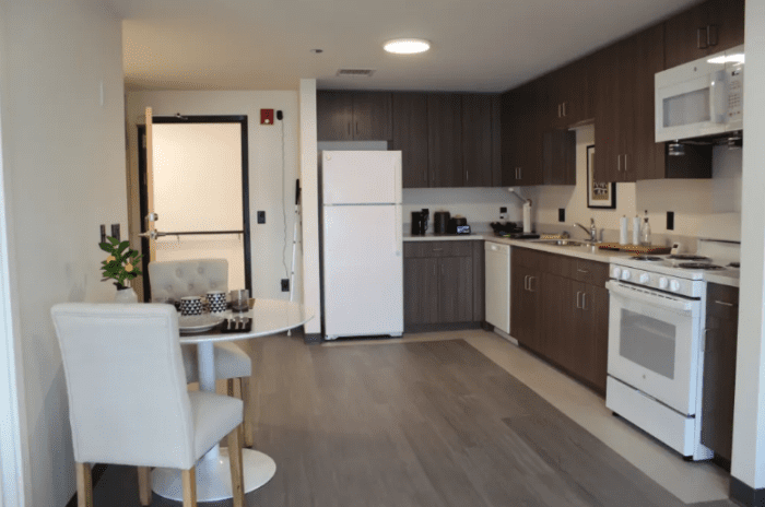 The kitchen and dining area of an accessible apartment featuring high color contrast refrigerator, oven, microwave, and dishwasher.