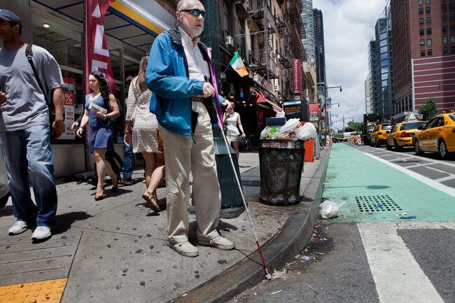 Image showing a blind man with his white cane at a crosswalk getting ready to cross a busy city street. Image showing a blind man with his white-cane at a crosswalk getting ready to cross a busy street