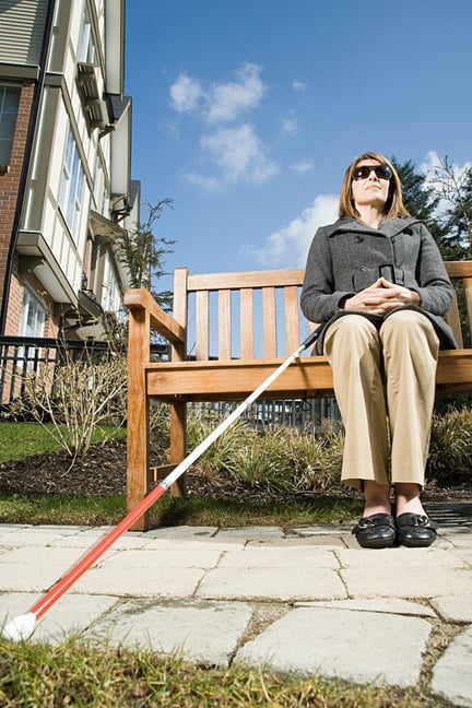 A woman who is blind sitting on a bench with her white cane next to her.