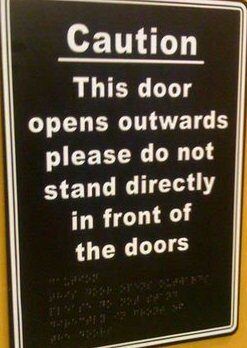 A print and braille sign that says "Caution. This door opens outwards, please do not stand directly in front of the doors." A print and braille sign that says "Caution. This door opens outwards, please do not stand directly in front of the doors."