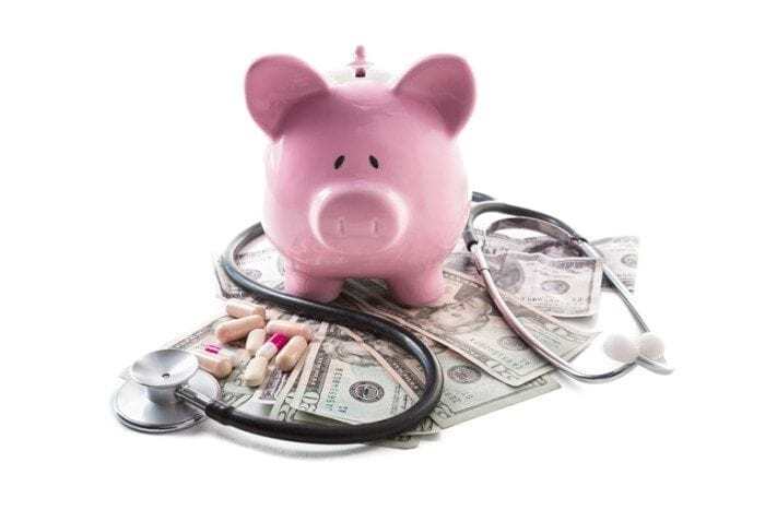 Piggy bank, medication and stethoscope resting on pile of dollars Piggy bank, medication and stethoscope resting on pile of dollars