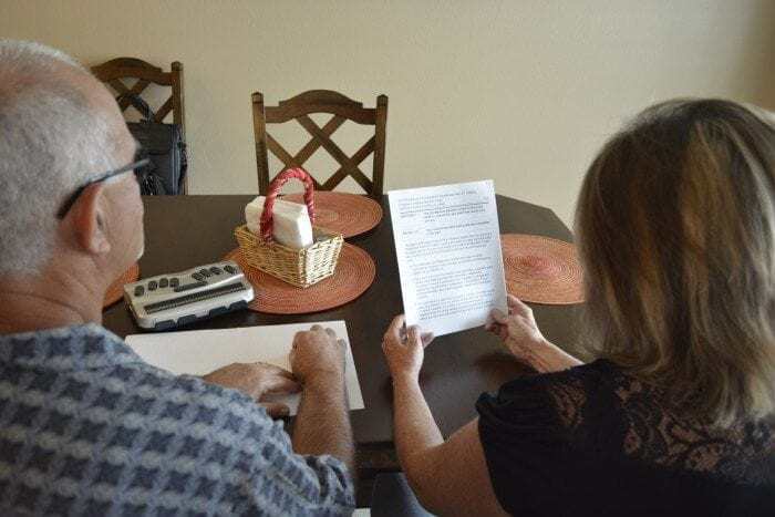 Image showing an over-the-shoulder view of a man and woman sitting the their kitchen table reading Braille and Large Print documents. Image showing an over-the-shoulder view of a man and woman sitting the their kitchen table reading Braille and Large Print documents.