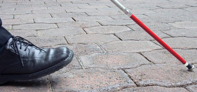 Image showing a close-up view of a persons shoe and White Cane while walking on a sidewalk Image showing a close-up view of a persons shoe and White Cane while walking on a sidewalk