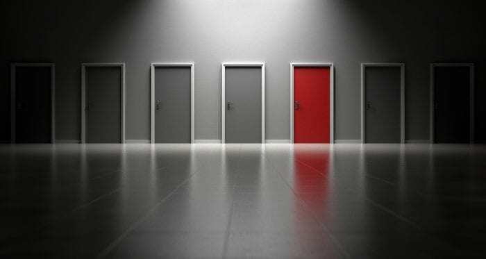 7 closed doors in an empty room with 1 door a different color than the rest