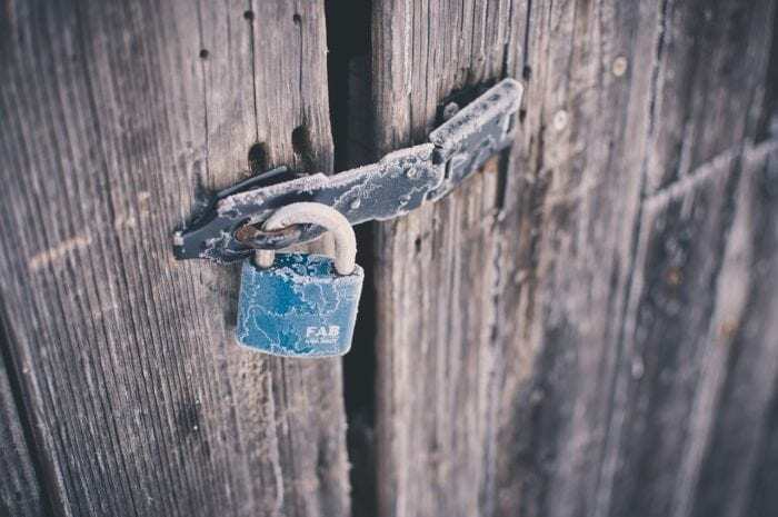 Padlock on wooden door that's frozen over with frost that prevents accessibility to the other side