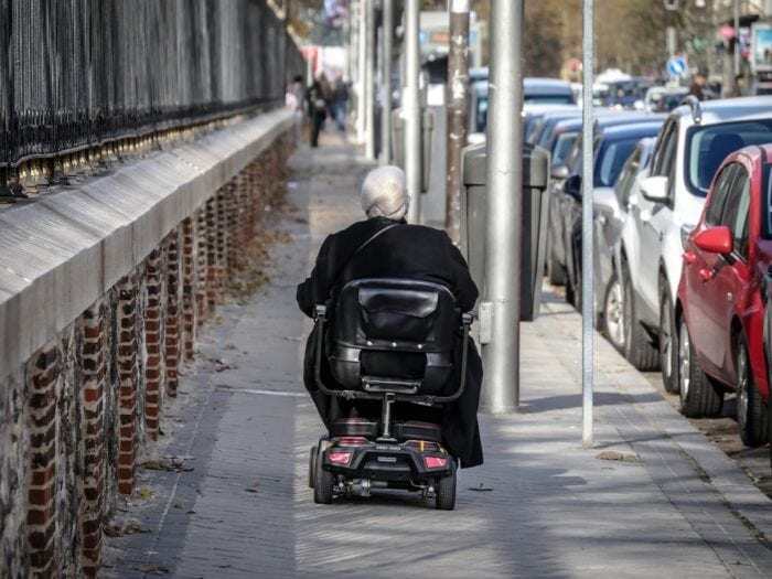 Person in motorized chair moving down a sidewalk
