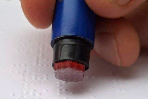 Fingers holding a Braille-tip pen over a braille document