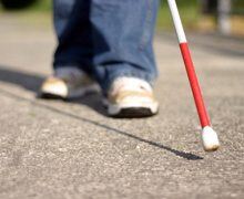 Image showing a close up view of the tip of a white cane while a person is walking down the sidewalk Image showing a close up view of the tip of a white cane while a person is walking down the sidewalk
